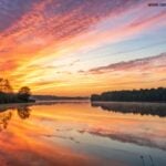Nascer do sol sereno sobre um lago calmo com cores vibrantes refletindo na água, simbolizando inspiração e energia para uma nova segunda-feira.