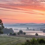 Cena tranquila de um amanhecer com um nascer do sol suave sobre uma paisagem pacífica, simbolizando um sábado abençoado e reflexão espiritual.