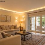 Sala de estar moderna com iluminação suave e tons claros nas paredes e móveis, criando uma atmosfera ampla e aconchegante.