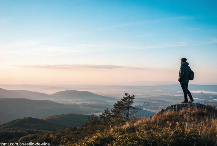 Uma paisagem serena com uma pessoa de pé no topo de uma montanha, contemplando um vasto horizonte.
