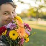 Uma pessoa sorrindo e segurando um buquê de flores coloridas em um parque.