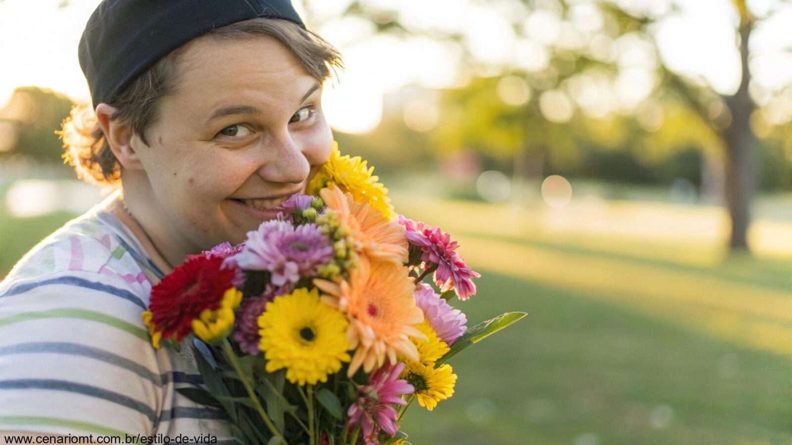 Uma pessoa sorrindo e segurando um buquê de flores coloridas em um parque.