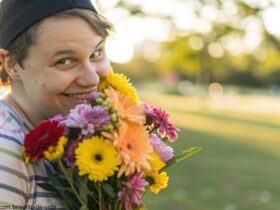 Uma pessoa sorrindo e segurando um buquê de flores coloridas em um parque.