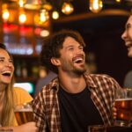 Grupo de amigos rindo em um bar enquanto alguém conta uma cantada engraçada