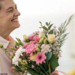 Cena romântica com uma pessoa sorrindo e segurando um buquê de flores.