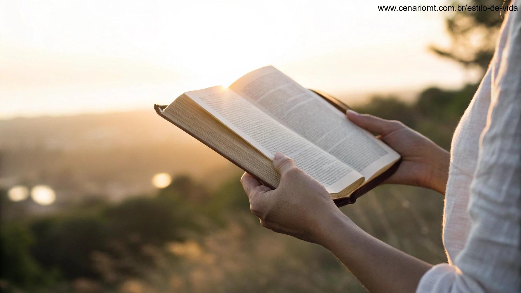 Mãos segurando uma Bíblia aberta ao ar livre durante o amanhecer, com raios de luz iluminando as páginas.