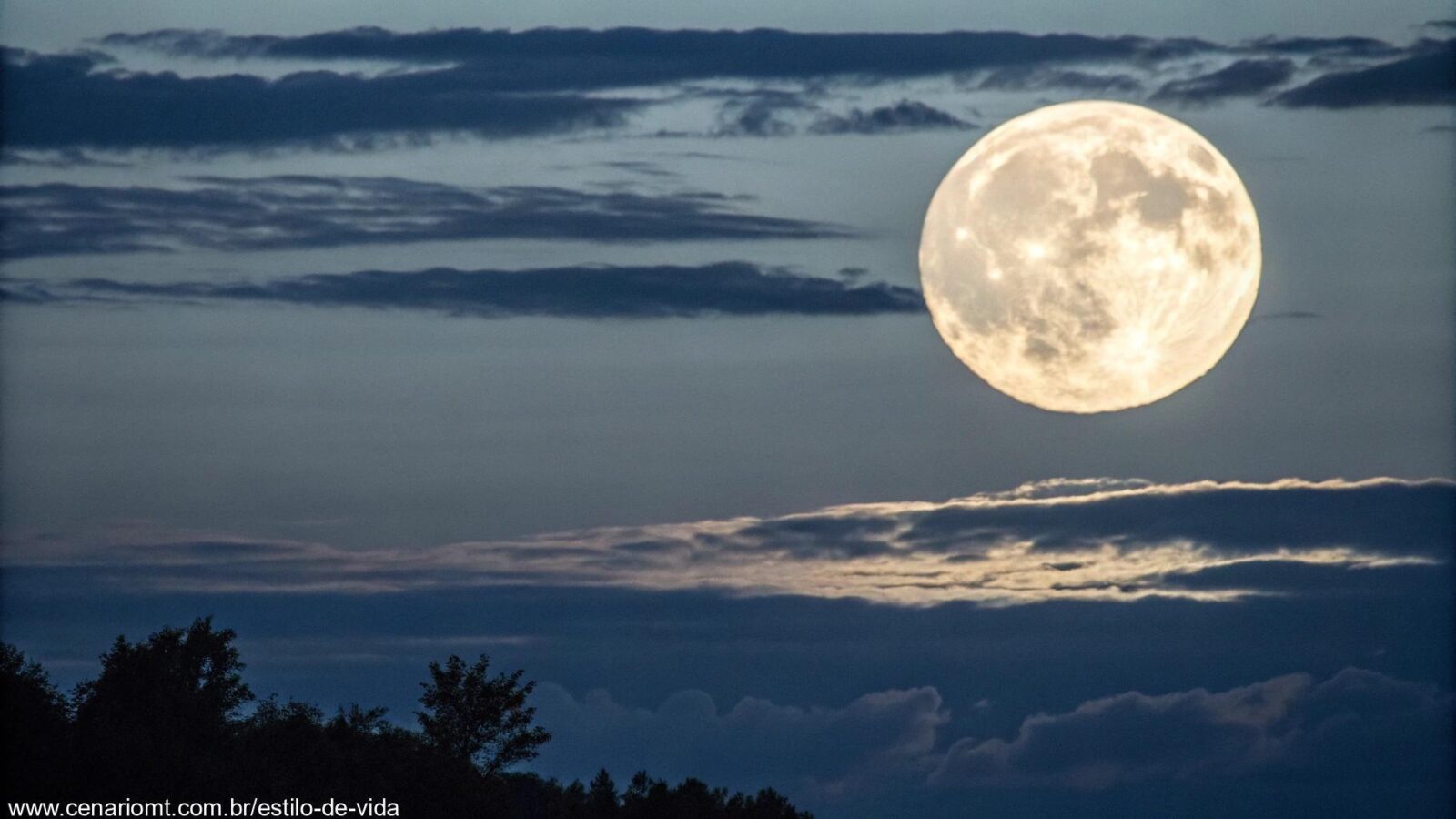 Uma vista clara de uma lua cheia brilhante no céu noturno com nuvens sutis ao redor.