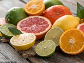 Frutas cítricas frescas dispostas sobre uma mesa rústica, incluindo laranjas, limões, limas e toranjas cortadas.