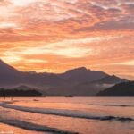 Amanhecer sereno sobre uma paisagem tranquila com montanhas e ondas suaves.