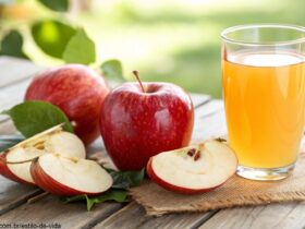 Uma maçã vermelha cortada sobre uma mesa de madeira com um copo de suco de maçã ao lado.