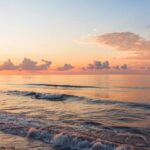 Imagem de um amanhecer sereno sobre o mar calmo, simbolizando esperança e fé para o dia.