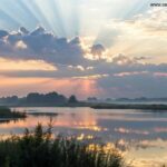 Paisagem serena ao amanhecer, com luz suave atravessando as nuvens, simbolizando paz e reflexão, com raios de luz suavemente destacando uma superfície de água calma.