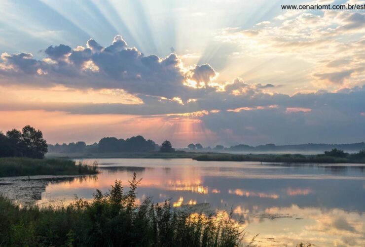 Paisagem serena ao amanhecer, com luz suave atravessando as nuvens, simbolizando paz e reflexão, com raios de luz suavemente destacando uma superfície de água calma.