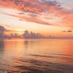 Amanhecer tranquilo sobre o oceano, com luz suave refletindo na água e uma atmosfera serena, simbolizando reflexão e fé.