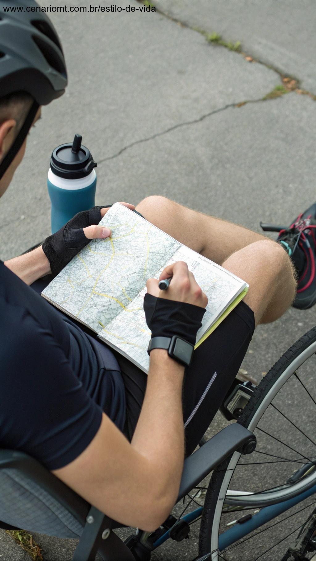 Ciclista anotando em um diário de treino, cercado por um mapa, uma garrafa de água e um relógio digital