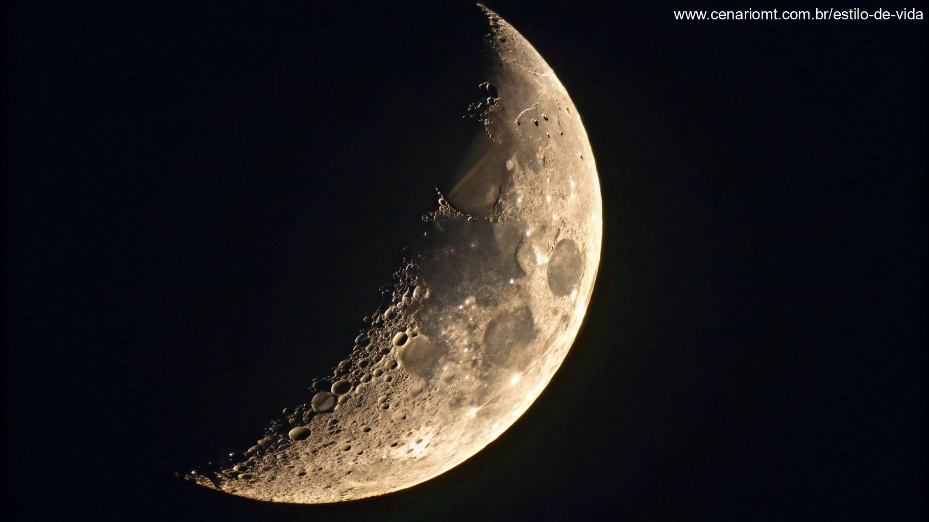 Close-up de uma lua crescente com uma fina faixa iluminada e o resto na sombra, em fundo escuro