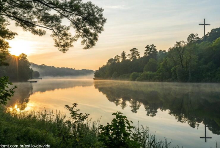 Nascer do sol sereno sobre um lago calmo com uma cruz refletida na água, cercado por vegetação exuberante e luz suave filtrando pelas árvores