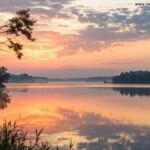 Paisagem tranquila com o nascer do sol sobre um lago calmo, transmitindo um ambiente de reflexão e espiritualidade.