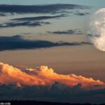Vista deslumbrante da Lua Gibosa Crescente no céu noturno, com nuvens suaves passando e um toque do brilho laranja do pôr do sol refletindo no horizonte.
