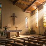 Interior de uma igreja tranquila com luz do sol entrando suavemente por vitrais, bancos de madeira e um altar simples adornado com uma cruz e velas