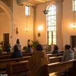 Interior tranquilo de uma igreja com luz suave, onde um grupo de pessoas está reunido em oração em uma manhã de domingo, refletindo sobre os ensinamentos espirituais.
