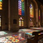 Cena tranquila de um interior de igreja com luz suave vindo através das janelas de vitrais, destacando a reflexão da liturgia do dia.