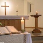Imagem de um altar de igreja com uma Bíblia e uma vela acesa, simbolizando a reflexão diária para a liturgia de segunda-feira.
