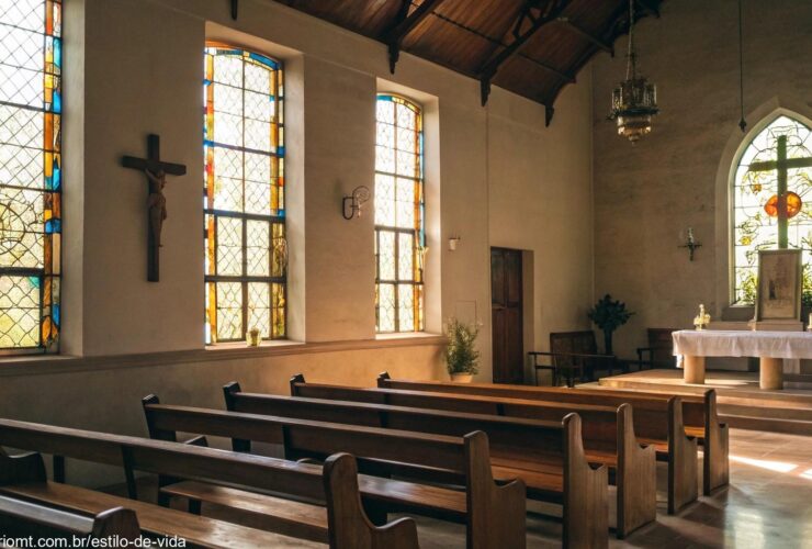 Interior de uma igreja serena com luz suave passando pelos vitrais, bancos de madeira e um altar simples com uma cruz
