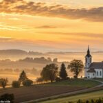 Amanhecer tranquilo sobre uma igreja no campo, com luz dourada iluminando o céu.