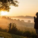 Nascer do sol tranquilo com luz dourada sobre um campo sereno, uma mulher em oração.