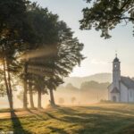 Cena de manhã tranquila com luz suave do sol e uma igreja ao fundo, simbolizando esperança e fé.