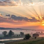 Uma paisagem tranquila ao amanhecer, com raios suaves iluminando o ambiente, simbolizando um novo começo e renovação espiritual.