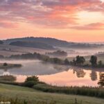 Cena serena de manhã com o nascer do sol sobre uma paisagem tranquila, transmitindo positividade e tranquilidade, ideal para uma mensagem de esperança e inspiração para a manhã de sexta-feira.