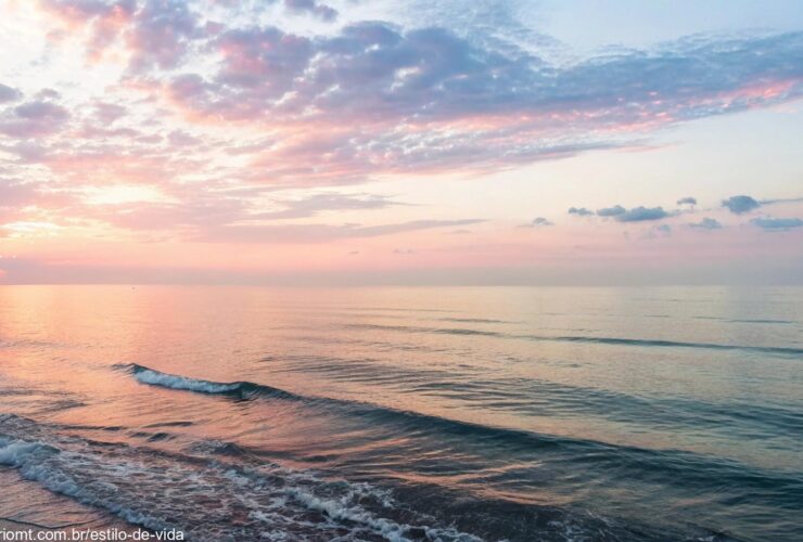 Uma imagem serena de um amanhecer tranquilo sobre o mar, com cores suaves no céu e ondas calmas refletindo a luz do sol.