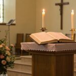 Altar de igreja sereno e tranquilo com uma Bíblia aberta, rodeada por velas e flores.