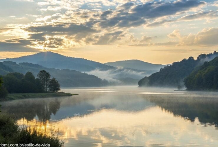 Paisagem tranquila de manhã com luz suave do sol, colinas cobertas de névoa e águas calmas refletindo o céu.