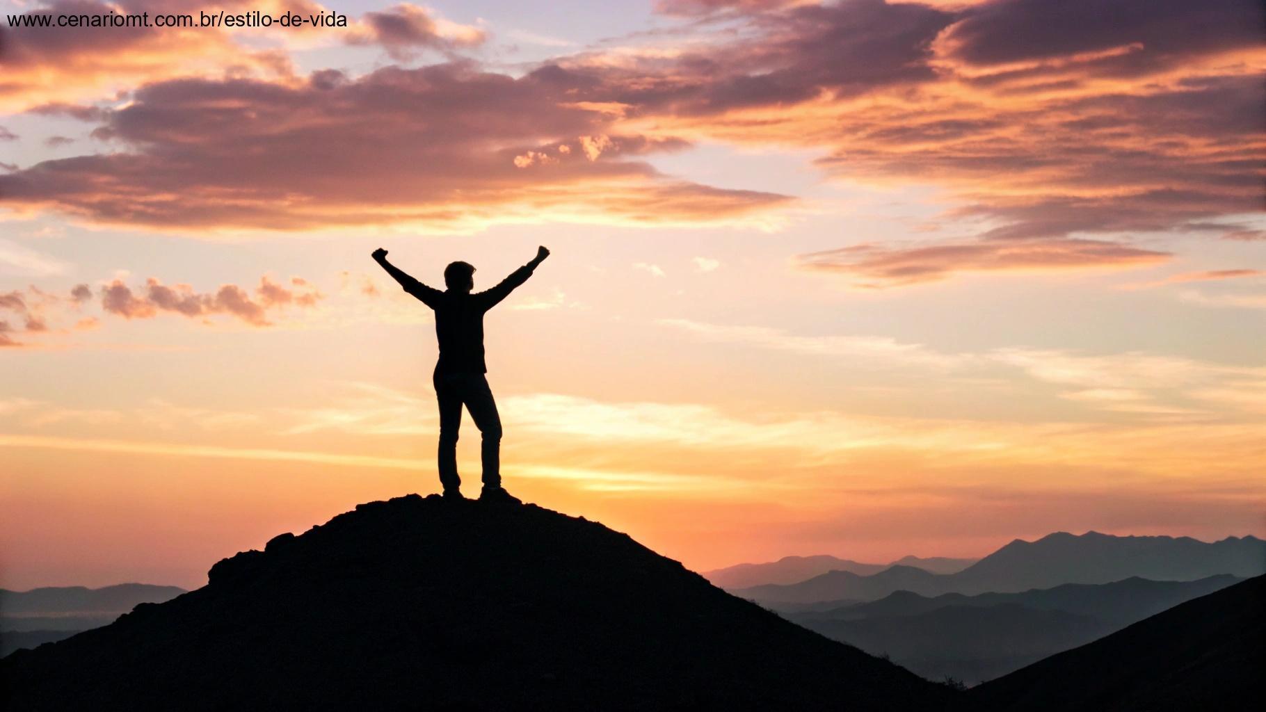 Pessoa no topo de uma colina com os braços erguidos ao céu enquanto o sol nasce, representando motivação e sucesso.