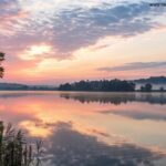 Imagem serena de um amanhecer sobre um lago calmo, simbolizando reflexão e fé.