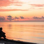Imagem de um amanhecer tranquilo sobre o oceano, simbolizando reflexão e oração no domingo de manhã.