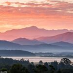 Amanhecer tranquilo sobre uma cadeia de montanhas, com tons suaves de rosa e laranja no céu, refletindo um começo de dia pacífico e cheio de esperança.