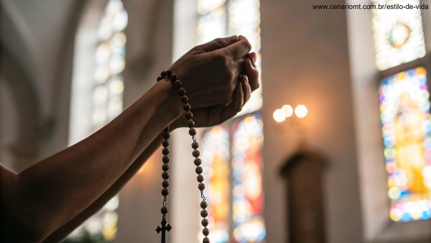 Um par de mãos segurando um terço com um fundo desfocado de um vitral de igreja