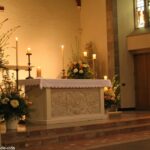 Cena pacífica de um altar de igreja, com velas acesas e flores, representando a reflexão do 'Santo do Dia: Domingo 09 03 2025 - Liturgia e Reflexão'.