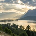 Paisagem serena com um nascer do sol sobre um lago calmo, cercado por montanhas.