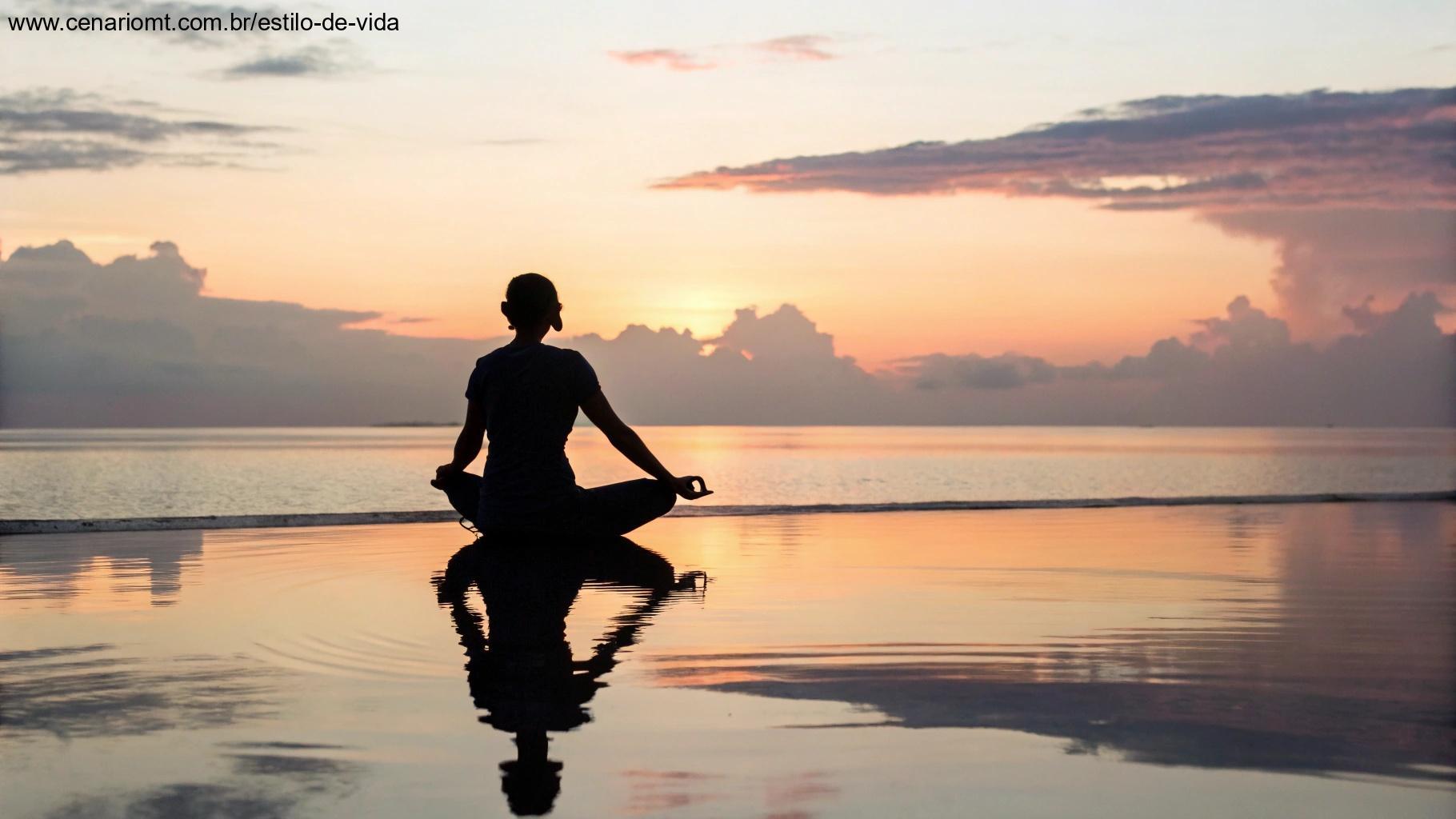 Nascer do sol tranquilo sobre águas calmas com silhueta de pessoa em pose de meditação