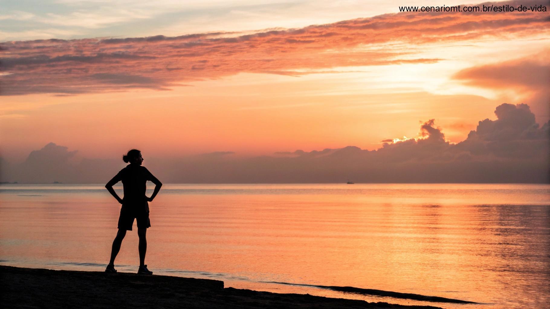 Um belo nascer do sol sobre um oceano calmo, com a silhueta de uma pessoa de pé com confiança, simbolizando fé e força para conquistar o dia.