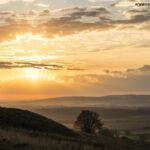 Paisagem ao amanhecer com uma cruz solitária em uma colina, simbolizando fé e reflexão espiritual