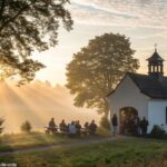 Imagem de uma capela ao amanhecer com fiéis em oração e luz suave