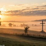 Amanhecer tranquilo no campo com cruz ao fundo simbolizando fé e esperança