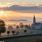 Imagem de um amanhecer pacífico sobre uma igreja, com raios suaves de luz sobre uma paisagem serena, simbolizando um novo começo e renovação espiritual.