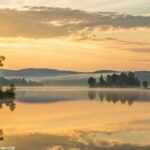 Inspiração para o dia com fé e serenidade, com um nascer do sol tranquilo sobre um lago calmo.